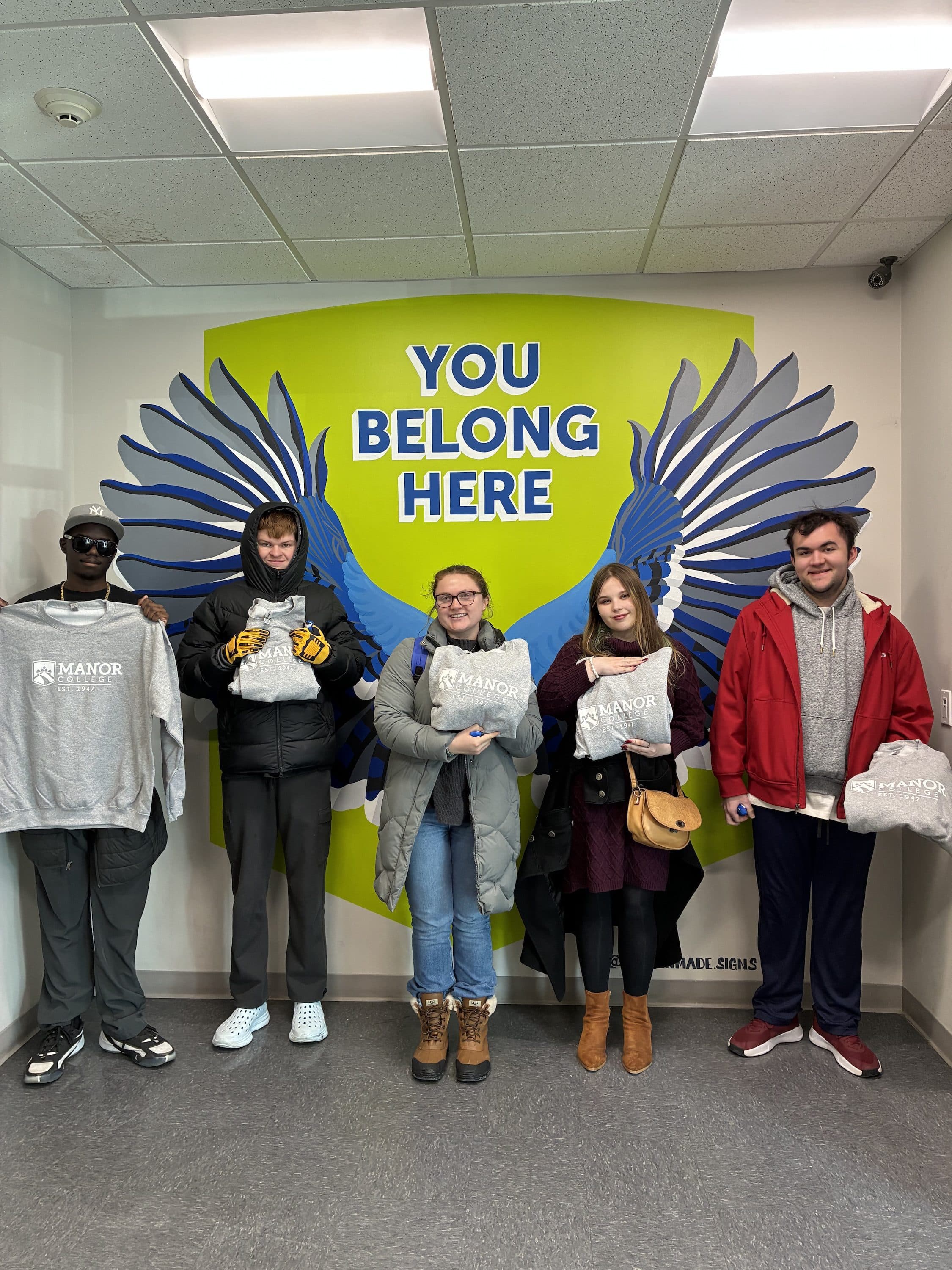 Students posing in front of a You Belong Here mural at Manor College