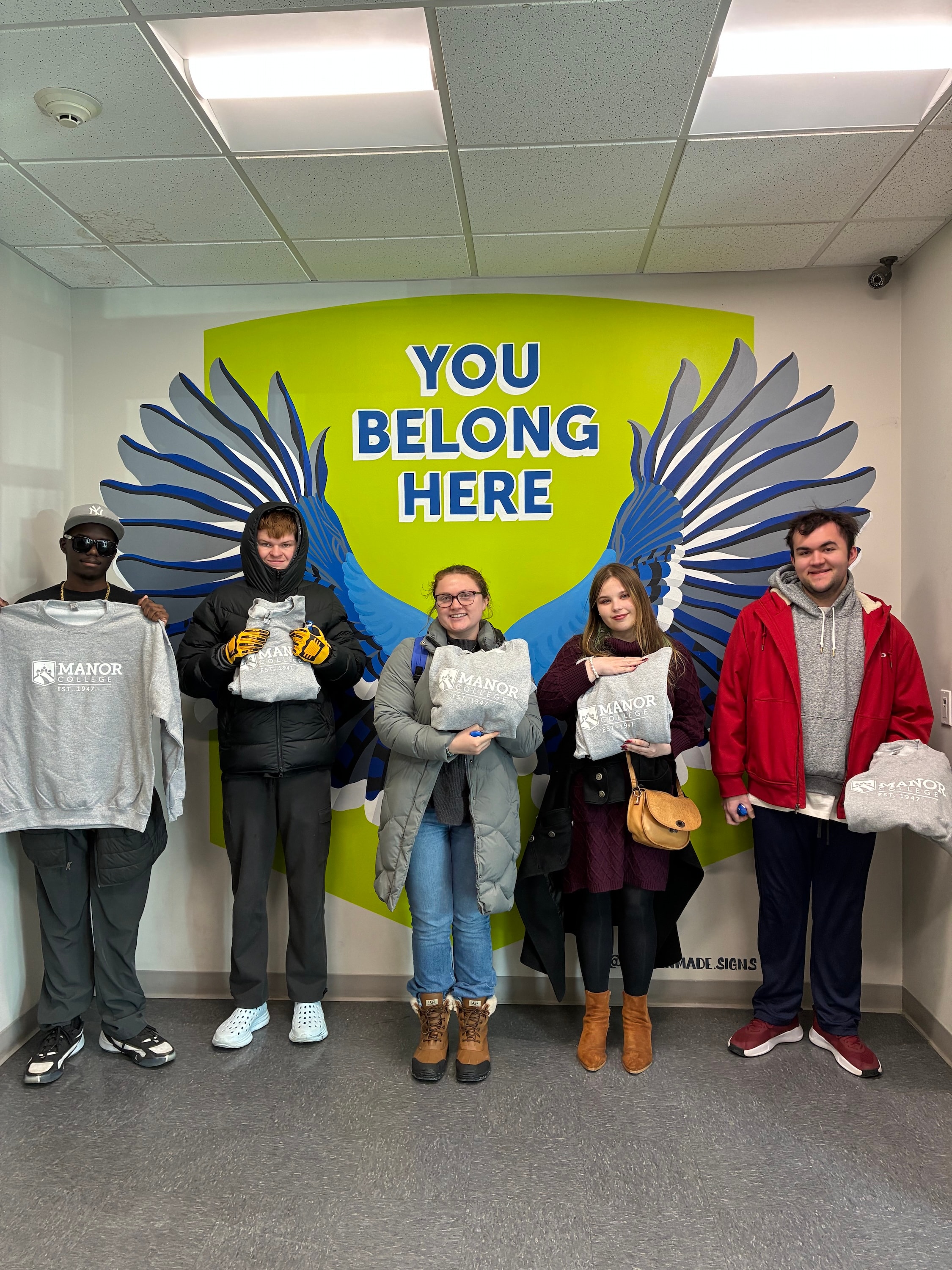 Students posing in front of a You Belong Here mural at Manor College
