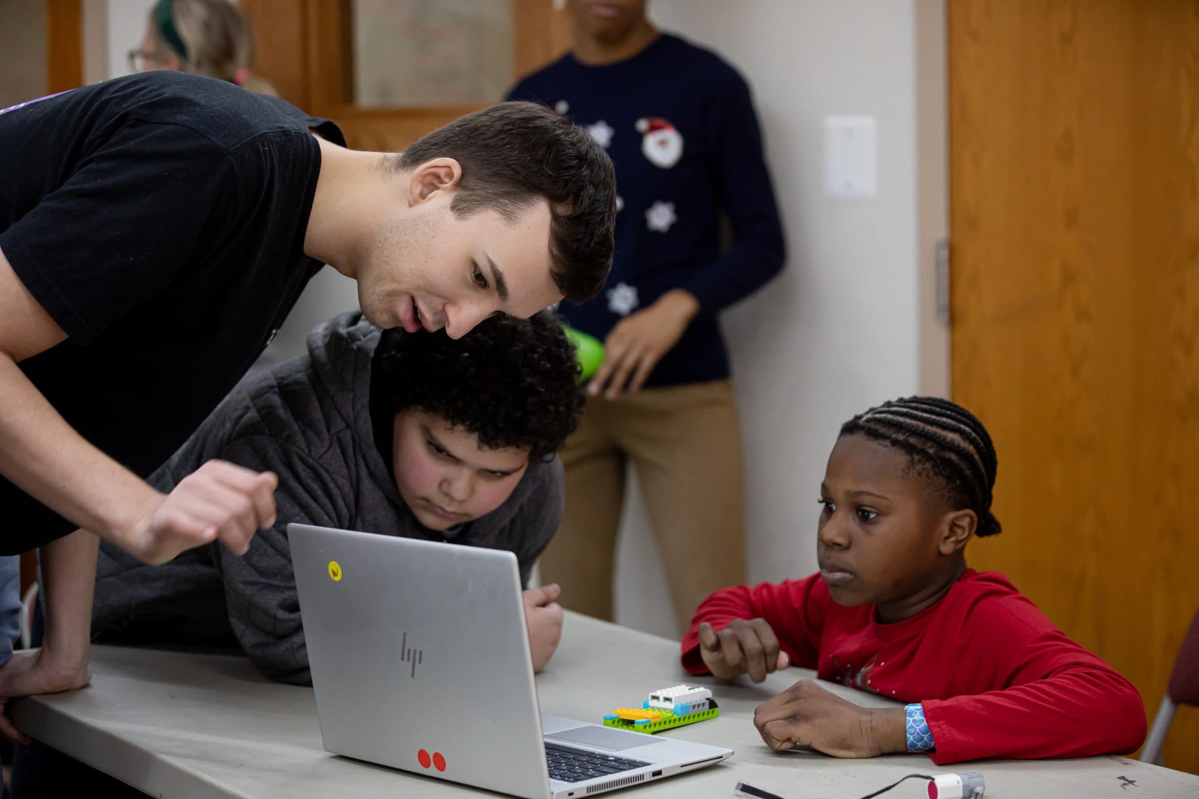 Teacher leaning over laptop with two students looking on