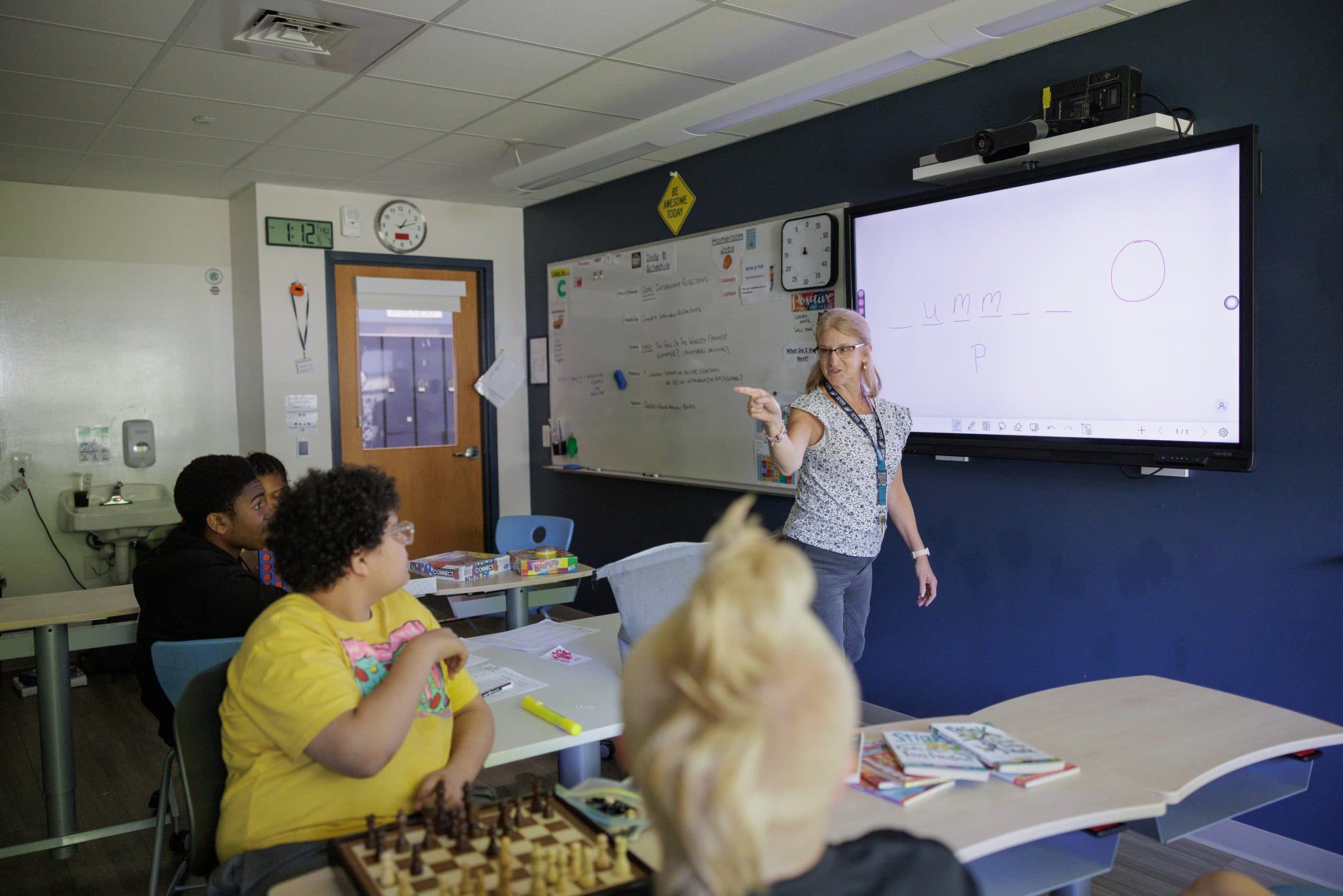Teacher writing on the whiteboard as a student works at their desk